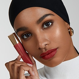 Model with a red lip, holding Estée Lauder Whipped Matte Liquid Lip with Moringa Butter in shade Hot Shot. 