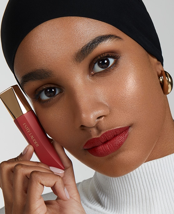Model with a red lip, holding Estée Lauder Whipped Matte Liquid Lip with Moringa Butter in shade Hot Shot. 