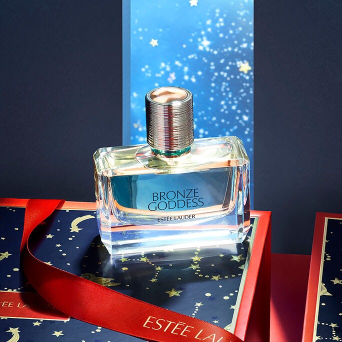 Estée Lauder Bronze Goddess fragrance displayed in a red and navy-blue scene with a starry background