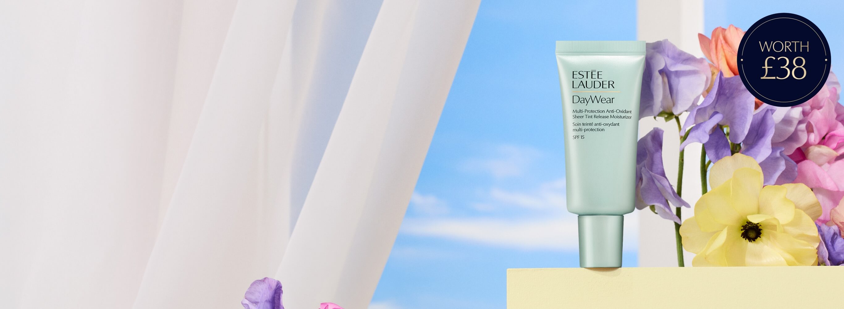 An Estée Lauder DayWear Sheer Tint Moisturiser on a blue sky background with flowers.