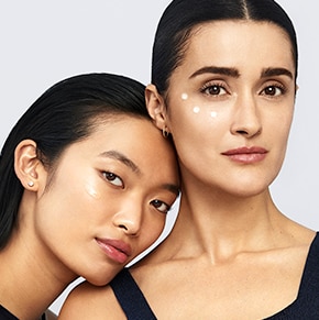 Two women trying on skincare on their cheekbones. 