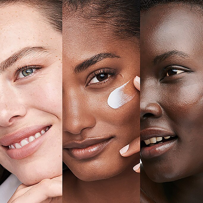 Three women smiling, the woman in the middle has added a moisturiser to her face. 