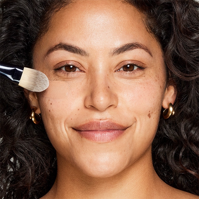 An image of a woman having her foundation applied with a brush